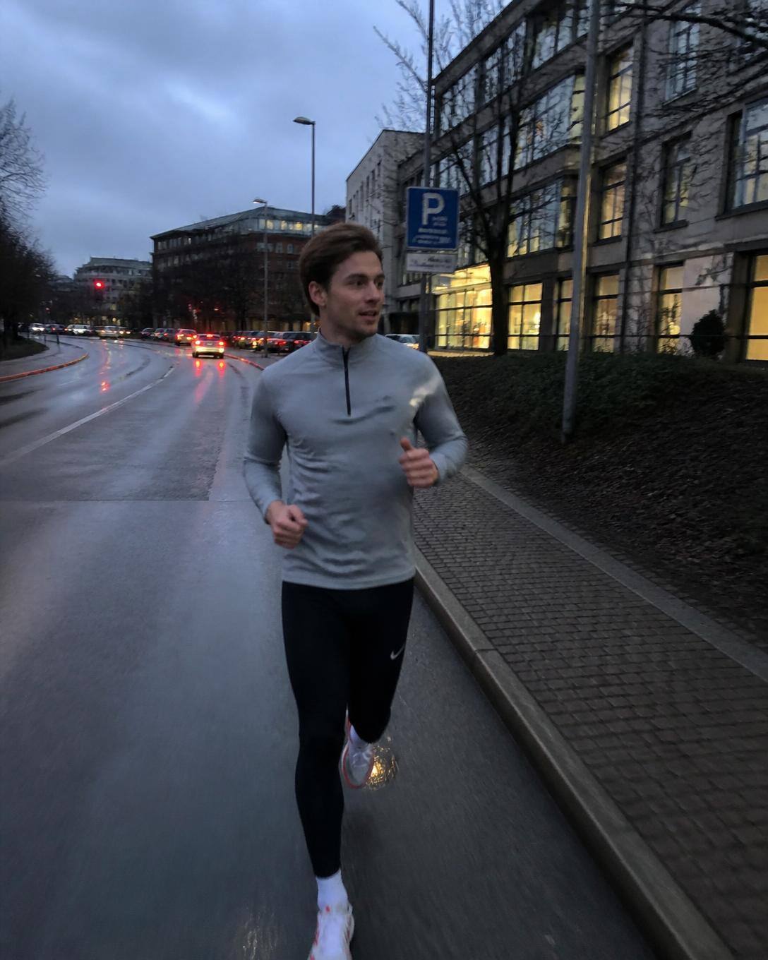 Löpare i svarta tights och grå half-zip på blöt stadsgata